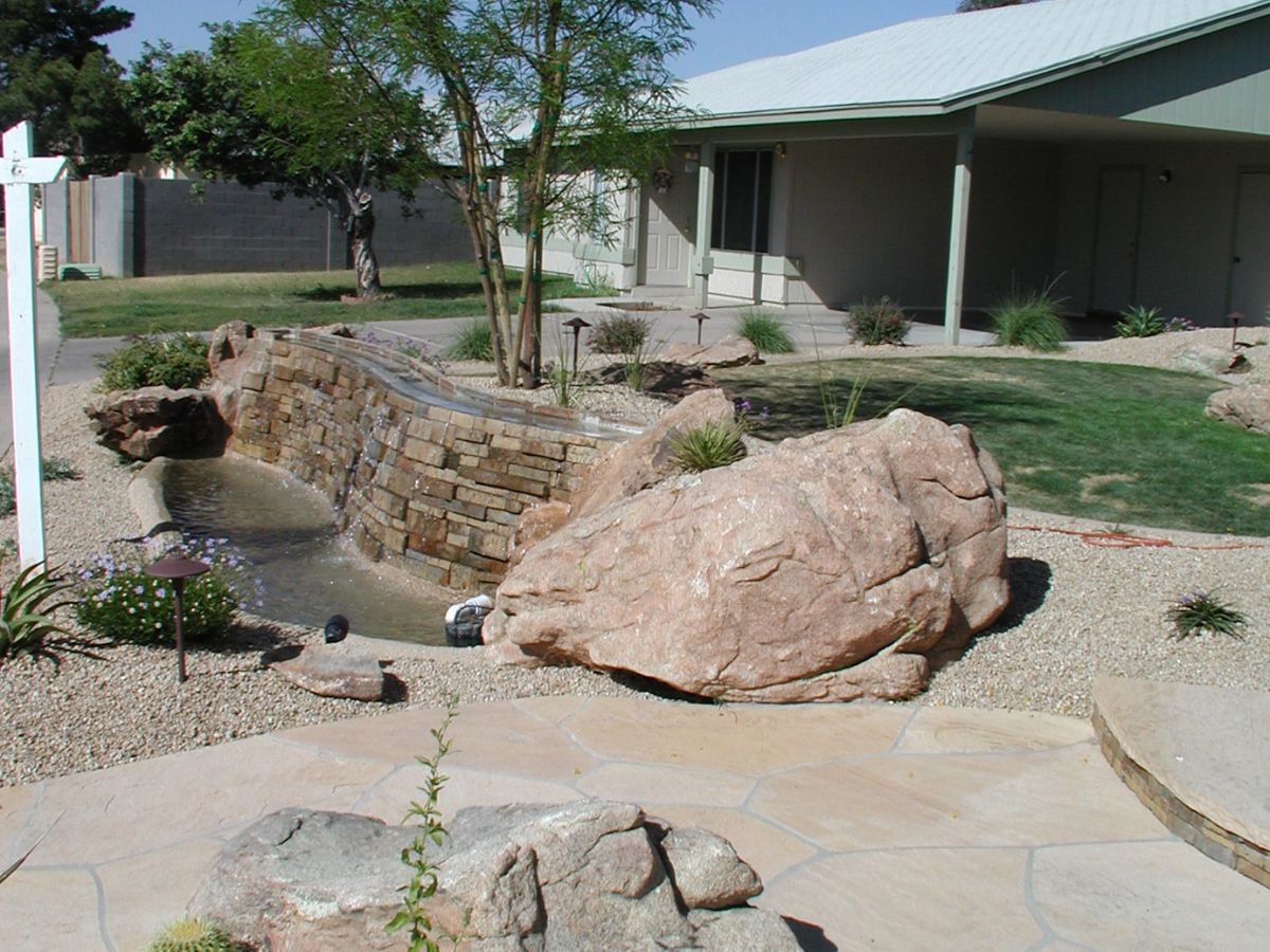 Stone waterfall feature in suburban backyard with large boulders, gravel xeriscape and flagstone patio.