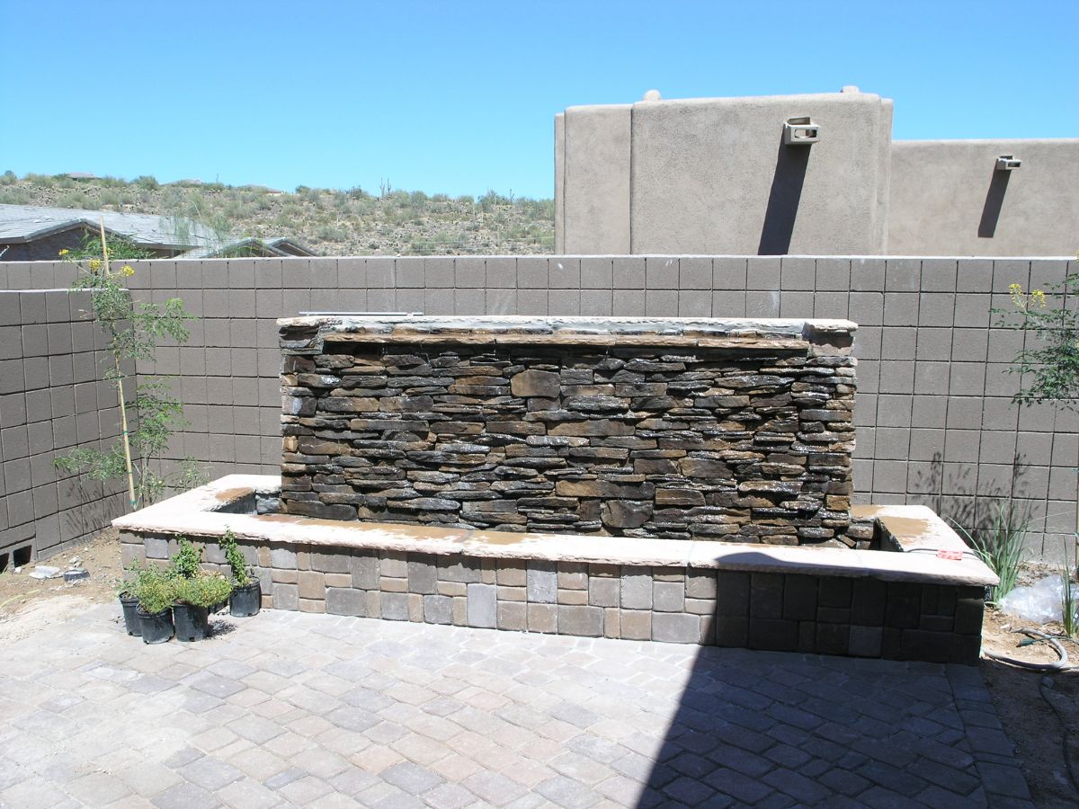 Backyard stacked stone water fountain and bench on paver patio with desert landscaping and privacy wall