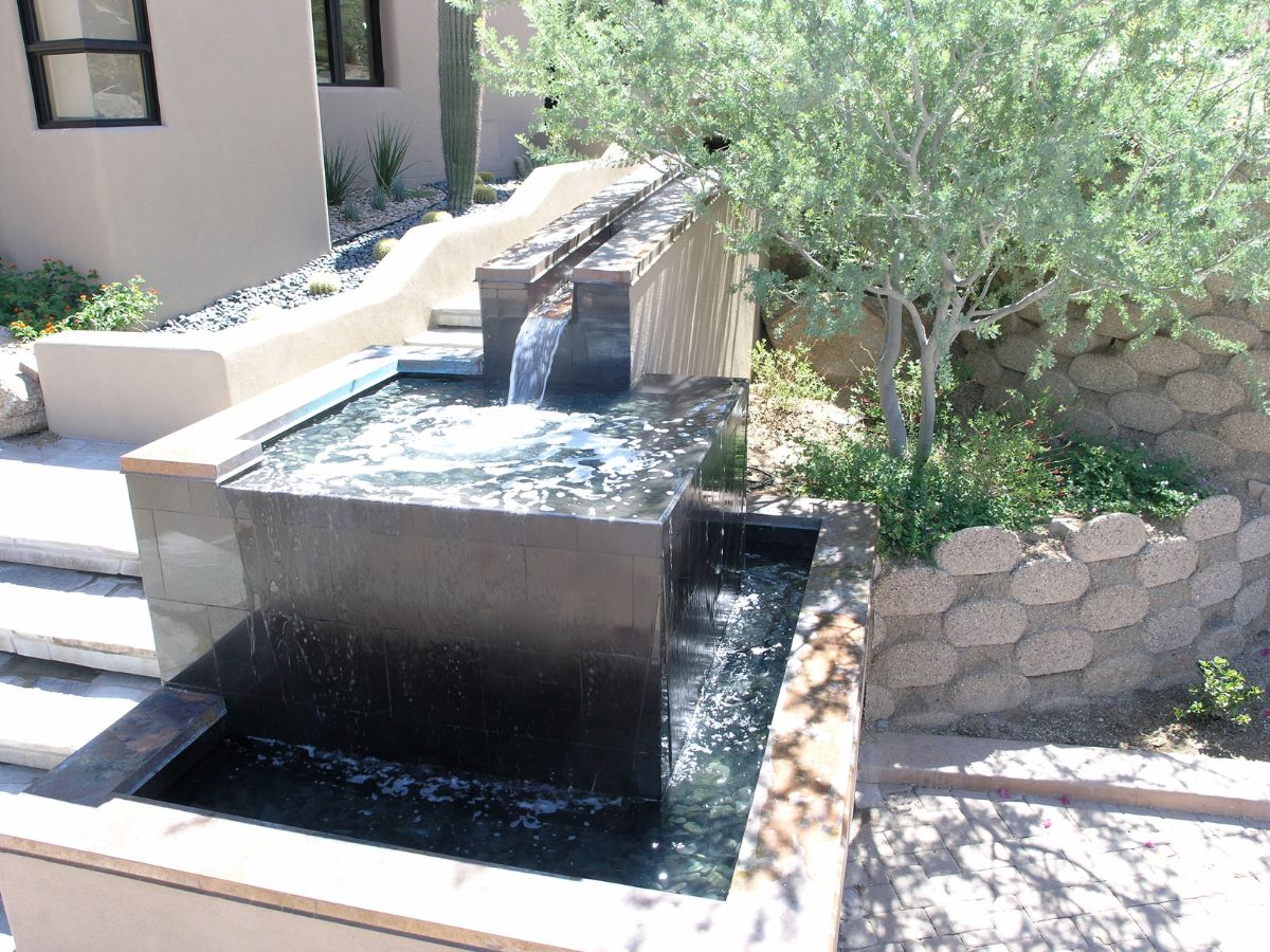 Modern tiered backyard water feature with cascading waterfall, dark stone fountain, desert landscaping and paved patio