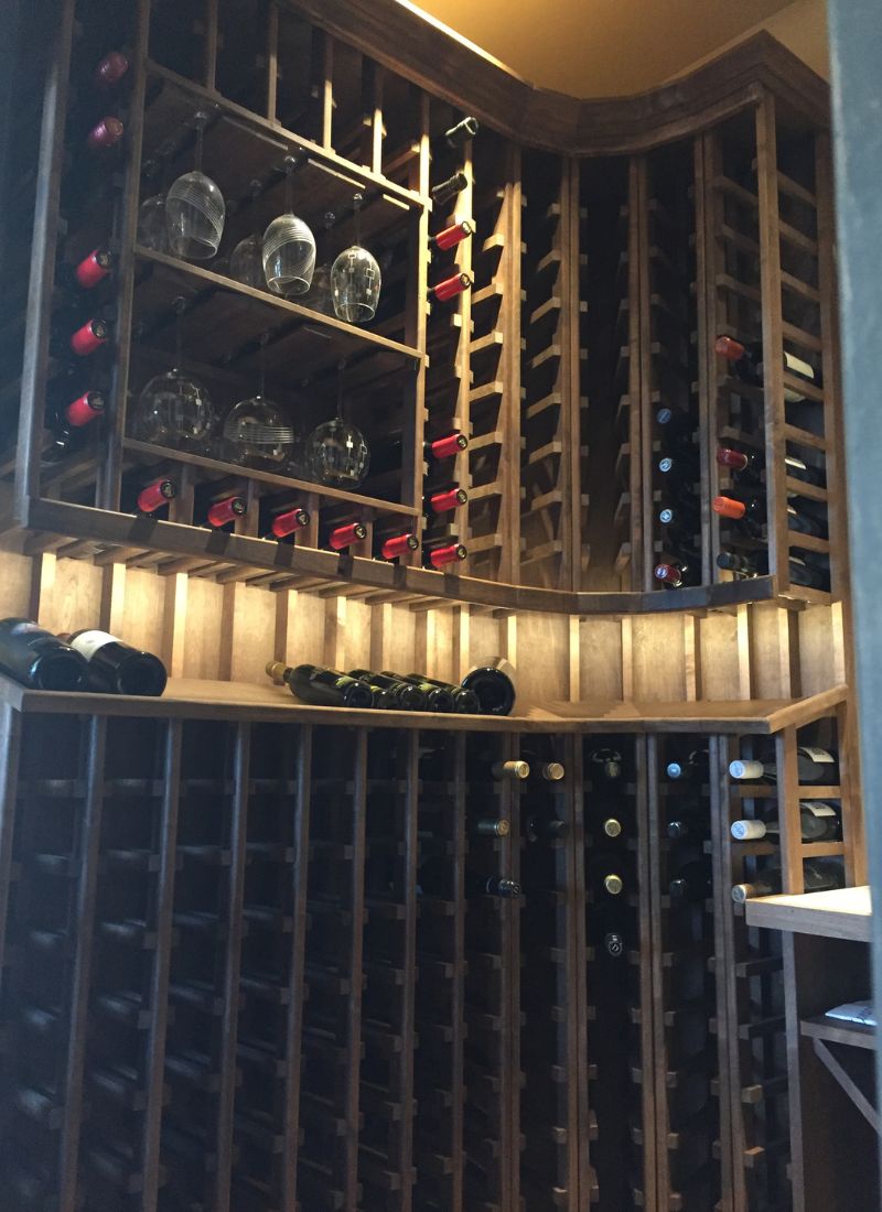 Built-in wooden wine cellar with vertical racks, red and white wine bottles and hanging wine glasses