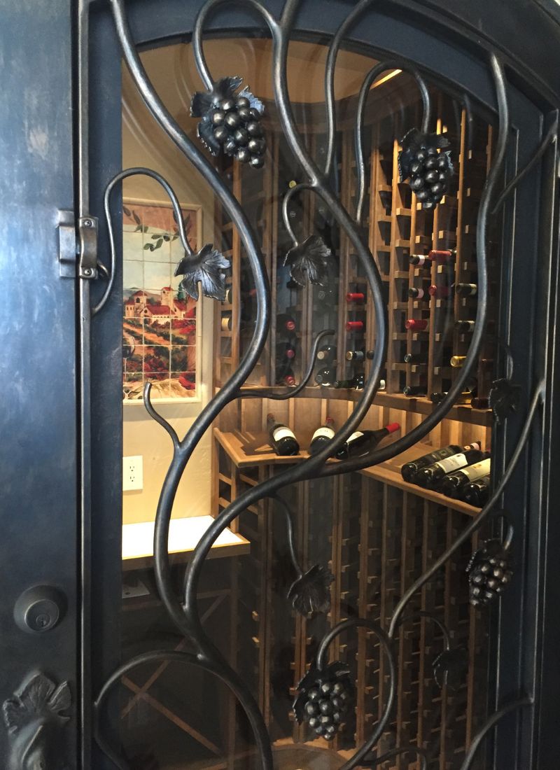 Wine cellar behind wrought-iron grapevine door: wooden racks and rows of stored wine bottles