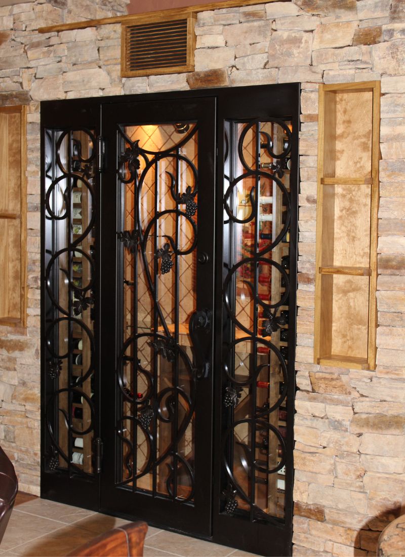 Wrought-iron and glass wine cellar door with ornate scrollwork set in rustic stone wall