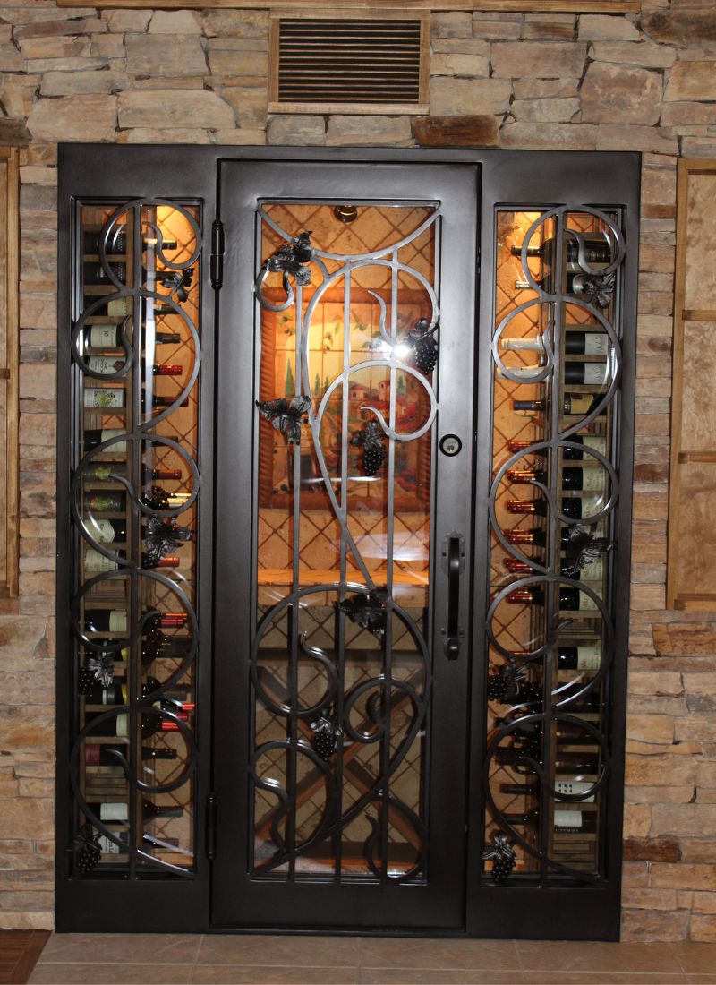 Ornate wrought-iron wine cellar door with grape-motif and vertical bottle racks in stone surround