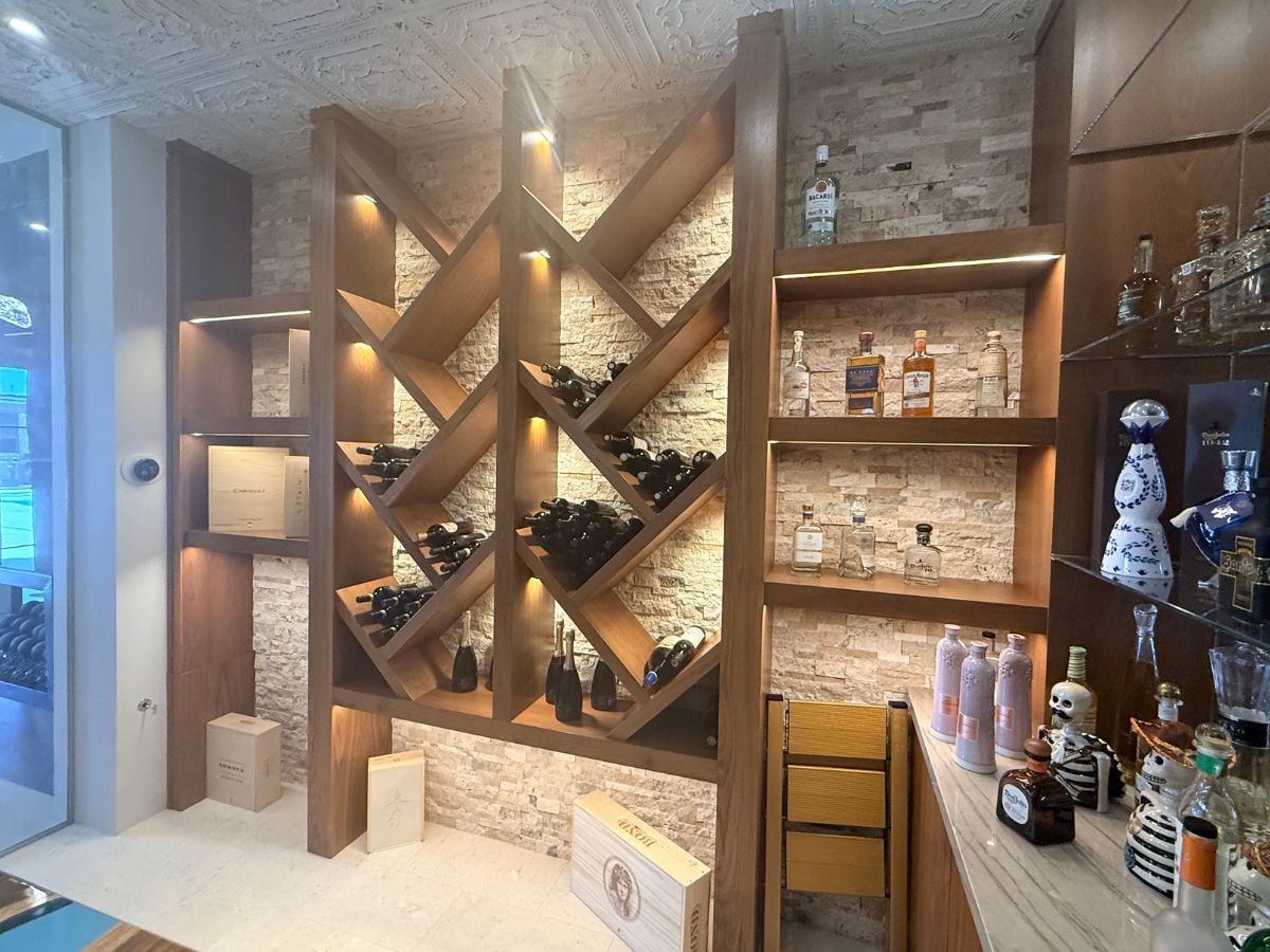 Wooden illuminated wine rack and liquor shelves in modern home bar wine cellar with assorted wine and spirits bottles