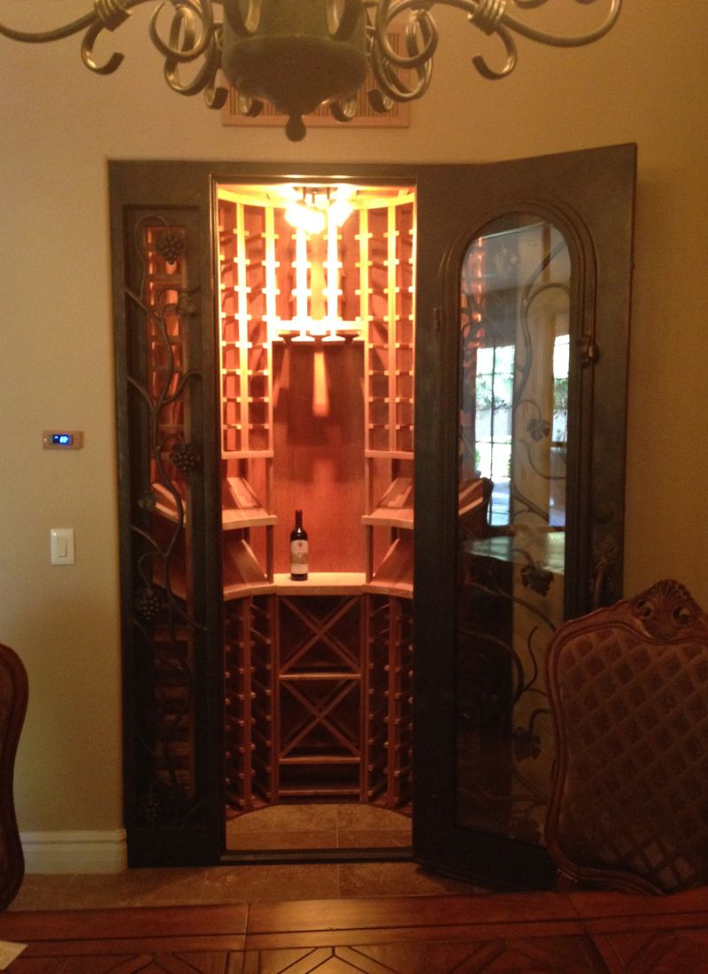 Elegant built-in wooden wine cellar with wrought-iron glass doors, illuminated bottle racks in dining room