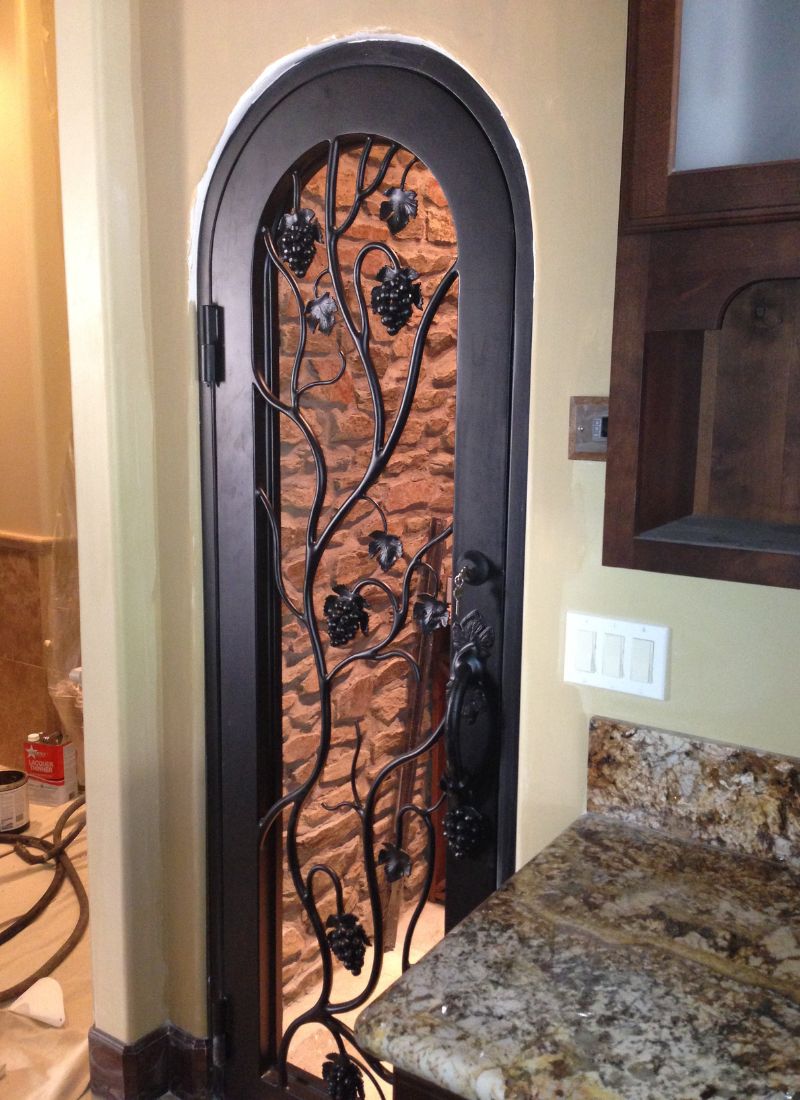 Arched wrought-iron grapevine wine cellar door with stone interior and adjacent kitchen granite countertop