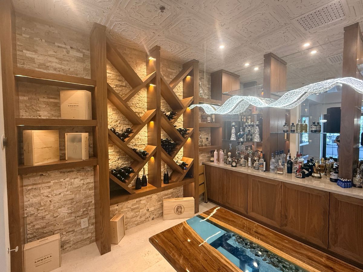 Luxury home wine cellar and bar with wooden diamond racks, stone accent wall, LED pendant light, epoxy river table