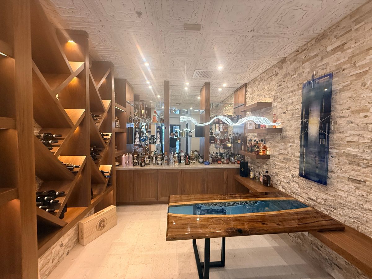 Luxury home bar with wooden wine rack, stone accent wall, illuminated shelving and epoxy river-style wood table.