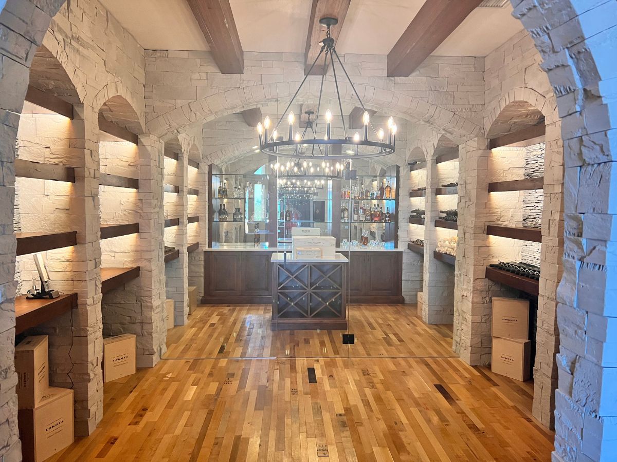 Luxurious wine cellar with stone archways, built-in wooden shelves, chandelier and hardwood floor showcasing wine storage.