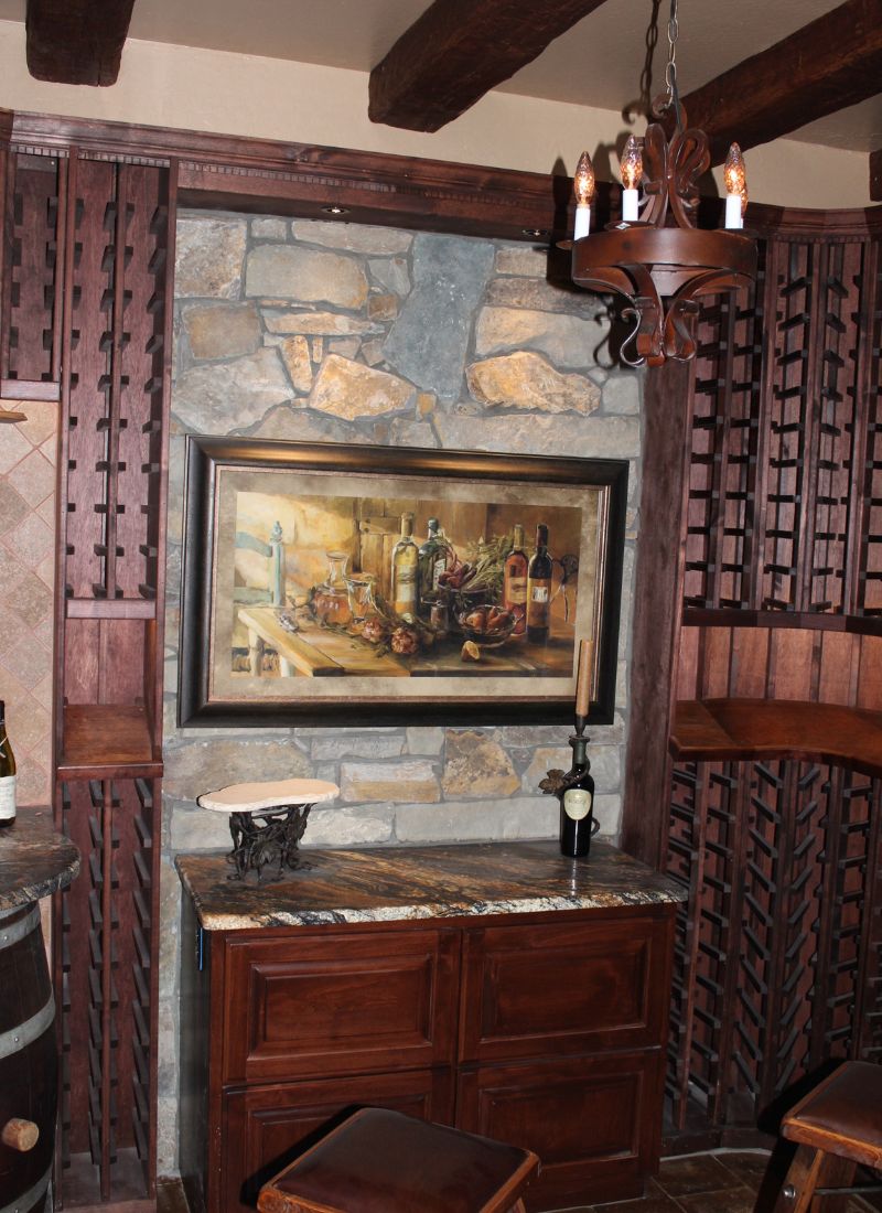 Wine cellar with stone wall, wooden wine racks, framed still-life painting, granite countertop and chandelier